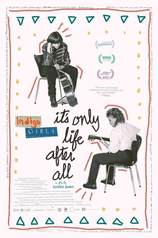 Promotional poster for "indigo girls: it's only life after all" set on a pale pink background with an image of Amy Ray on the top left corner and Emily Saliers on the bottom left. Both women are pictured sitting on a chair with a guitar.